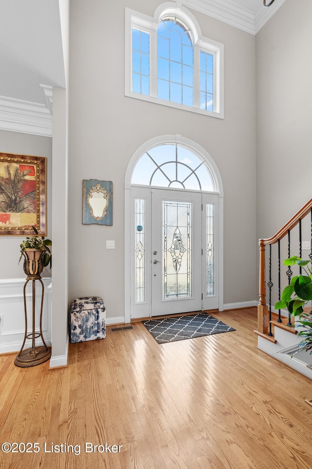 foyer entrance with ornamental molding, stairway, wood finished floors, and a wealth of natural light