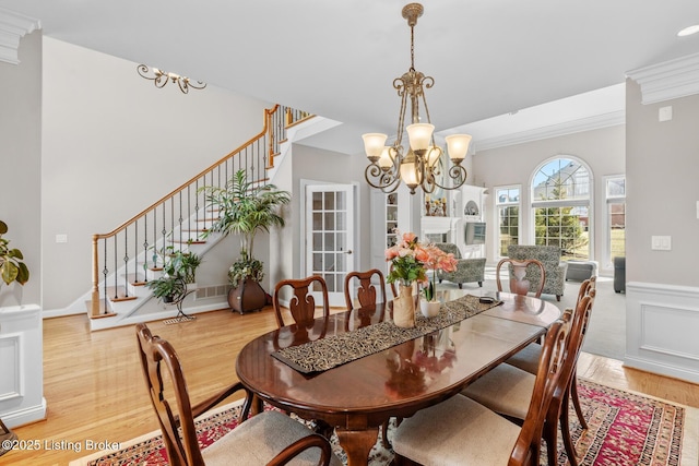 dining room featuring a chandelier, a wainscoted wall, light wood-style floors, stairway, and crown molding