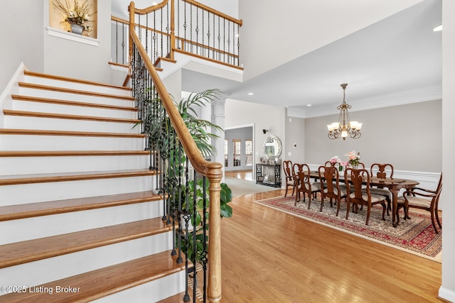 stairway with crown molding, recessed lighting, a high ceiling, wood finished floors, and a chandelier