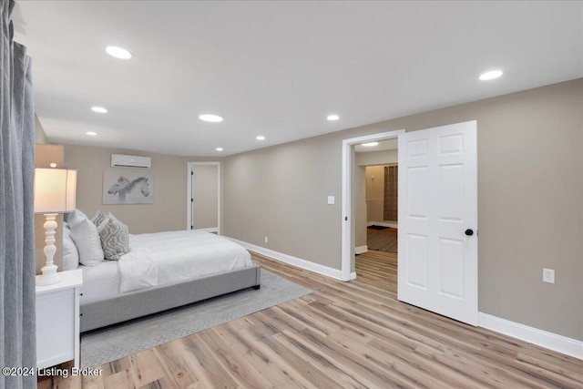 bedroom with a wall mounted AC and light hardwood / wood-style floors