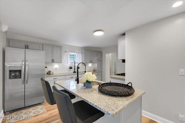 kitchen featuring stainless steel refrigerator with ice dispenser, a breakfast bar area, light stone counters, gray cabinets, and light hardwood / wood-style floors