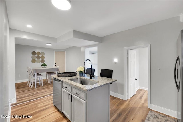 kitchen featuring sink, light hardwood / wood-style flooring, appliances with stainless steel finishes, a kitchen island with sink, and light stone countertops