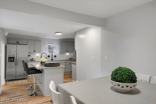 kitchen with a breakfast bar, gray cabinetry, a center island, stainless steel refrigerator with ice dispenser, and light wood-type flooring