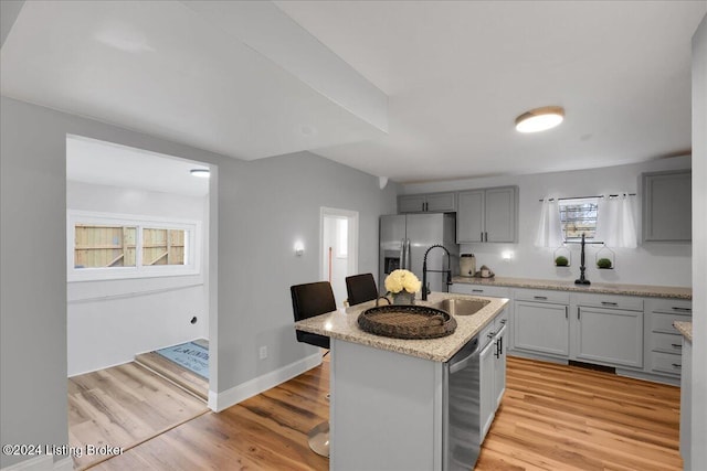 kitchen with wine cooler, sink, a center island with sink, light wood-type flooring, and stainless steel fridge