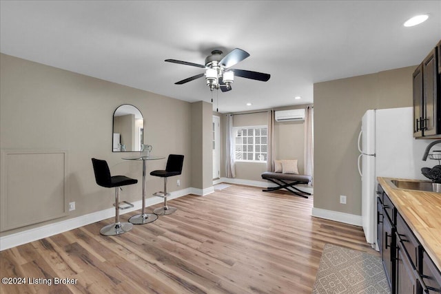 kitchen with sink, wooden counters, dark brown cabinets, a wall mounted air conditioner, and light wood-type flooring