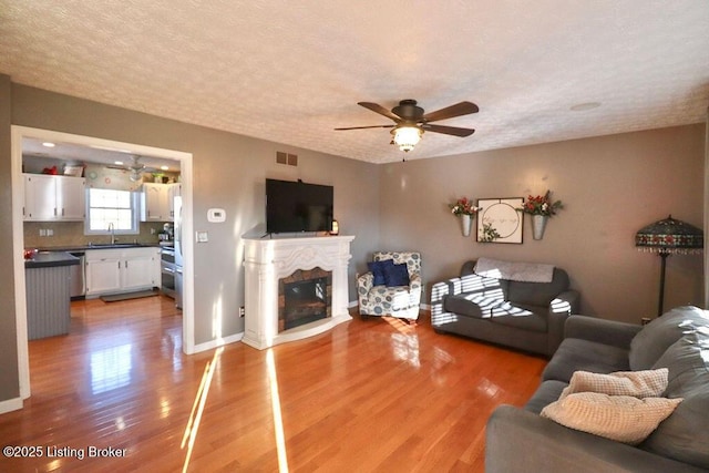 unfurnished living room featuring sink, hardwood / wood-style flooring, a textured ceiling, and ceiling fan