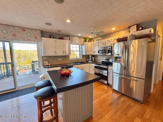 kitchen with sink, a breakfast bar, appliances with stainless steel finishes, white cabinetry, and a center island