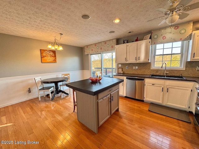 kitchen featuring stainless steel dishwasher, decorative light fixtures, a kitchen island, and light wood-type flooring