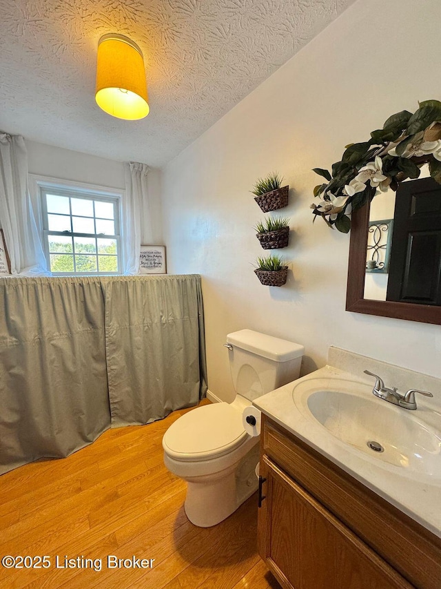 bathroom with wood-type flooring, vanity, a textured ceiling, and toilet