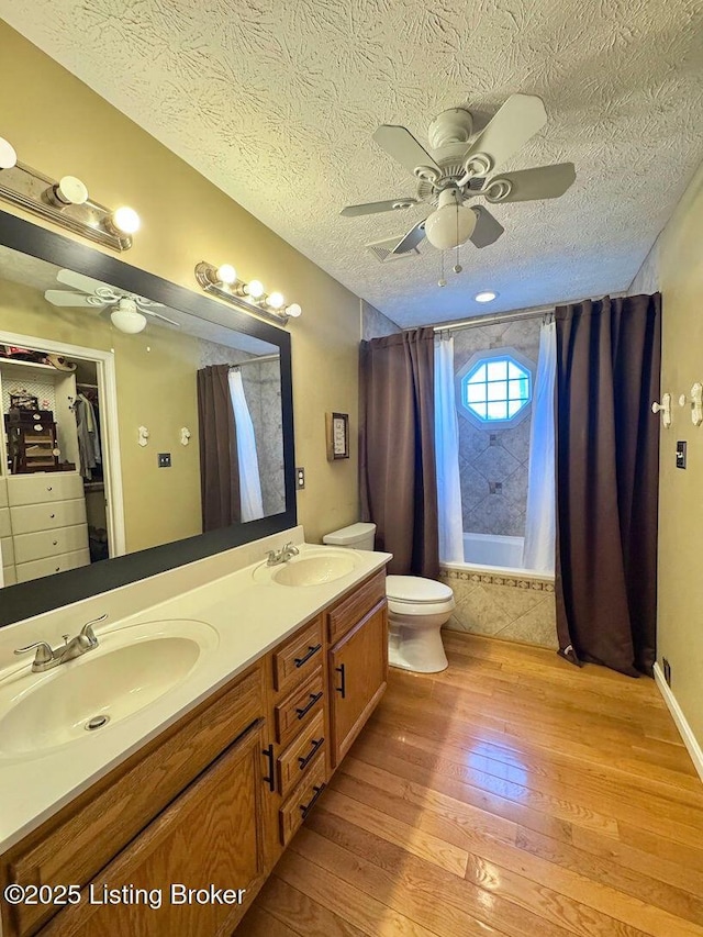 full bathroom with hardwood / wood-style flooring, vanity, ceiling fan, shower / bathtub combination with curtain, and a textured ceiling