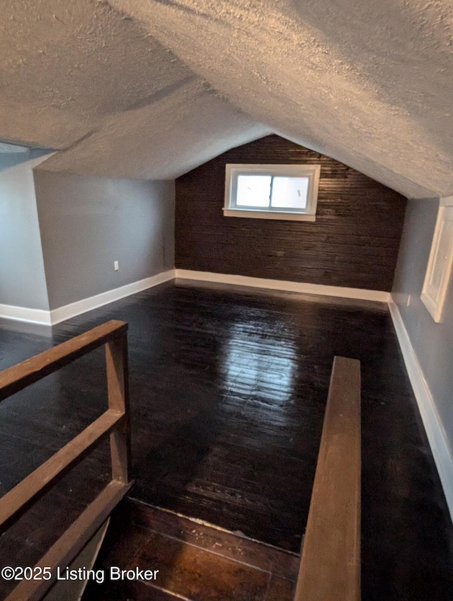 bonus room with dark wood-type flooring, lofted ceiling, and a textured ceiling