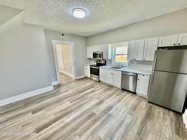 kitchen featuring sink, a textured ceiling, light hardwood / wood-style flooring, stainless steel appliances, and white cabinets