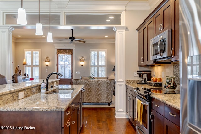 kitchen featuring sink, appliances with stainless steel finishes, light stone countertops, an island with sink, and ornate columns