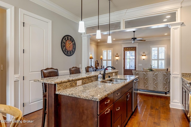 kitchen with ornate columns, pendant lighting, sink, a kitchen bar, and a kitchen island with sink