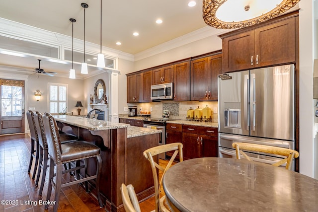 kitchen with decorative light fixtures, a center island with sink, stainless steel appliances, light stone countertops, and backsplash