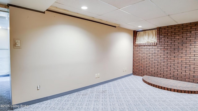 basement with carpet, a drop ceiling, and brick wall