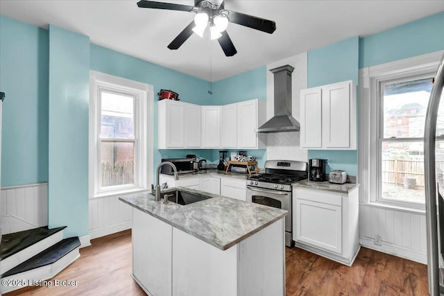 kitchen with stainless steel range with gas cooktop, white cabinetry, an island with sink, sink, and wall chimney range hood