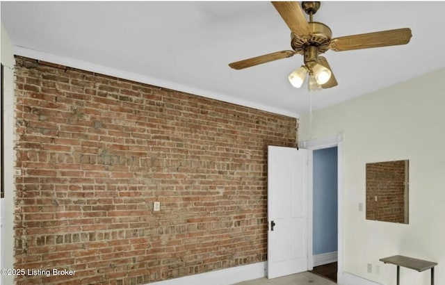 unfurnished room with ceiling fan and brick wall