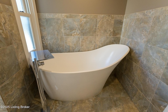 bathroom with a tub to relax in, tile walls, and a wealth of natural light