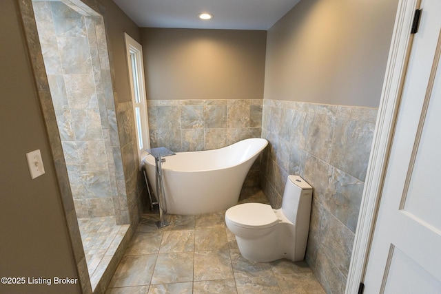 bathroom with a tub to relax in, toilet, and tile walls