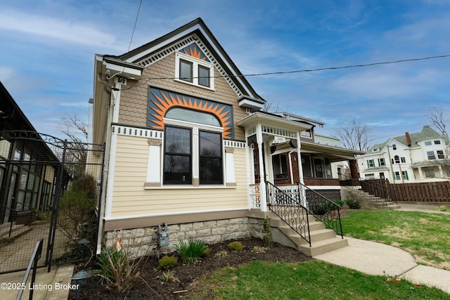 victorian-style house featuring a front yard, covered porch, and fence