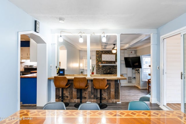 kitchen with stainless steel electric range oven, a breakfast bar area, backsplash, dark hardwood / wood-style flooring, and ceiling fan