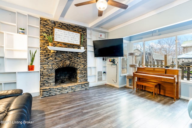 living room featuring beamed ceiling, wood-type flooring, a stone fireplace, and ceiling fan