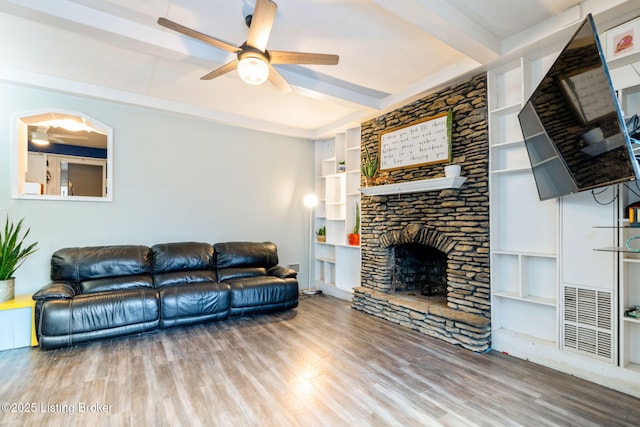 living room featuring a stone fireplace, beamed ceiling, hardwood / wood-style flooring, ceiling fan, and built in shelves