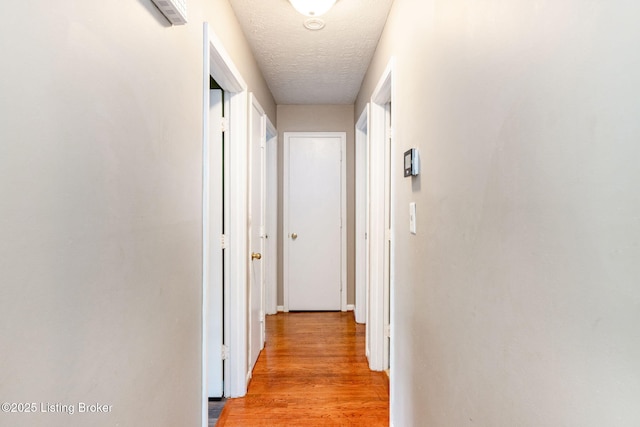 corridor with a textured ceiling and light wood-type flooring