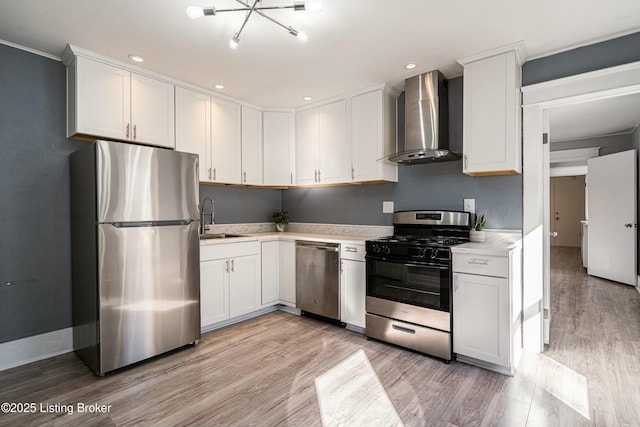 kitchen with wall chimney range hood, sink, appliances with stainless steel finishes, white cabinets, and light wood-type flooring