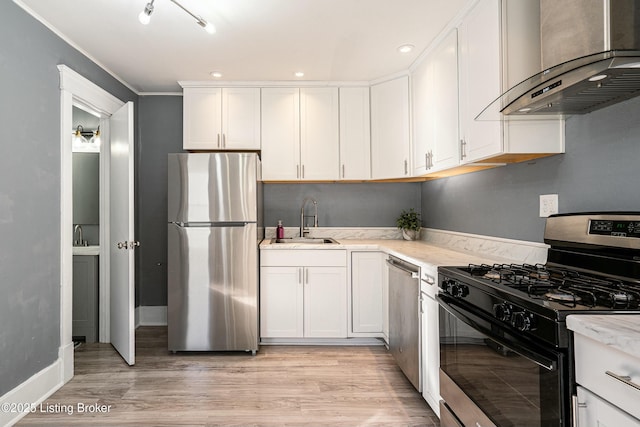 kitchen featuring sink, light wood-type flooring, appliances with stainless steel finishes, wall chimney range hood, and white cabinets