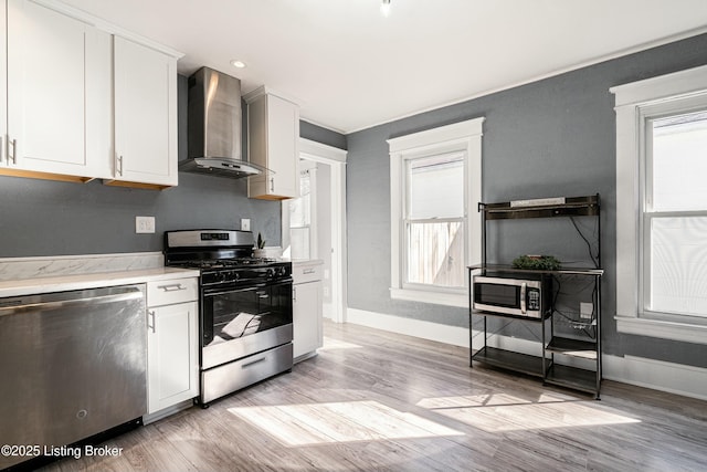 kitchen with white cabinetry, appliances with stainless steel finishes, a wealth of natural light, and wall chimney range hood