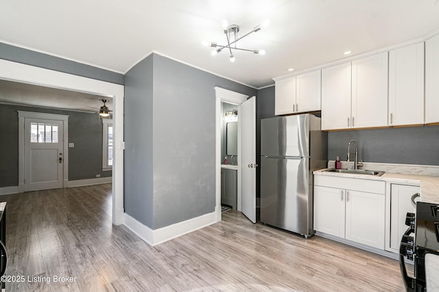 kitchen with sink, white cabinets, stainless steel fridge, ornamental molding, and light hardwood / wood-style flooring