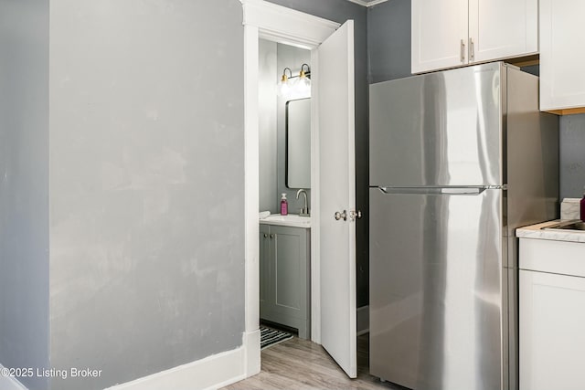 kitchen with white cabinetry, stainless steel fridge, sink, and light hardwood / wood-style flooring