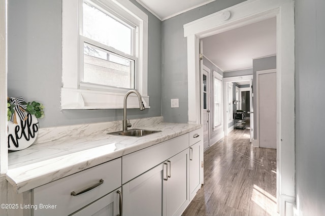 bar featuring sink, white cabinets, hardwood / wood-style flooring, crown molding, and light stone countertops