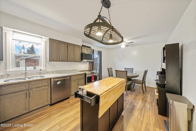 kitchen with sink, light stone counters, decorative light fixtures, stainless steel appliances, and light hardwood / wood-style floors