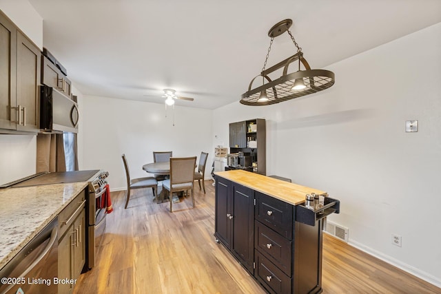 kitchen with light hardwood / wood-style flooring, appliances with stainless steel finishes, butcher block counters, dark brown cabinetry, and decorative light fixtures