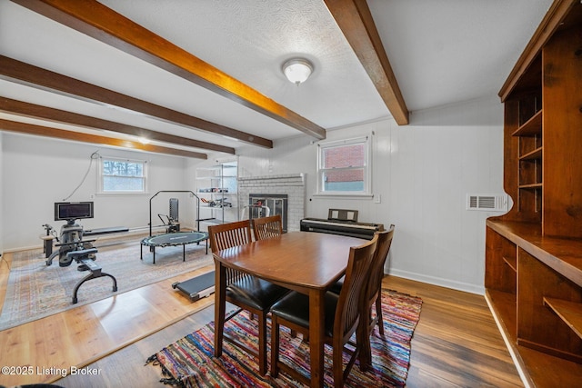 dining area featuring hardwood / wood-style flooring, a fireplace, a textured ceiling, and beamed ceiling