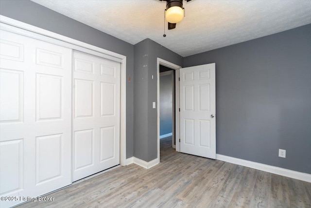 unfurnished bedroom with ceiling fan, a textured ceiling, a closet, and light wood-type flooring