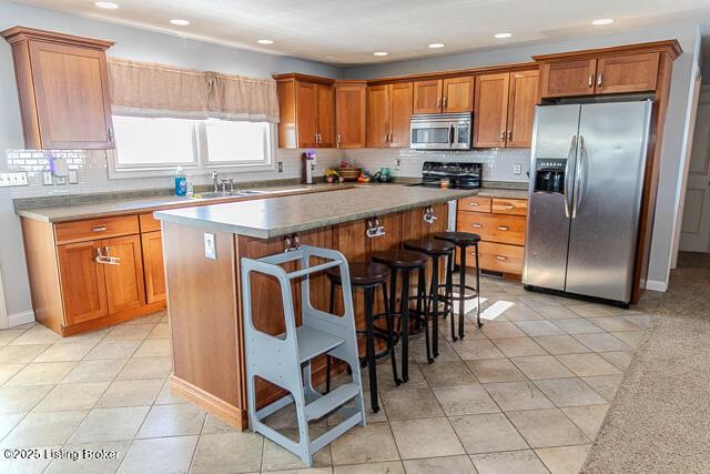 kitchen with a breakfast bar, a center island, light tile patterned floors, appliances with stainless steel finishes, and decorative backsplash