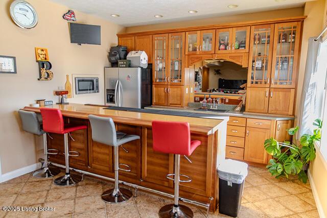 kitchen with sink, a kitchen breakfast bar, stainless steel refrigerator with ice dispenser, light tile patterned flooring, and kitchen peninsula