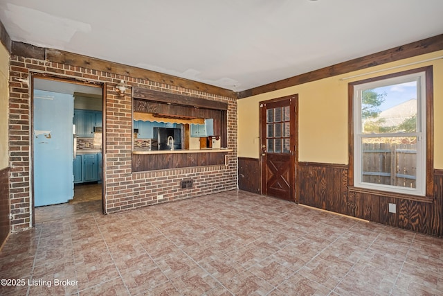 unfurnished living room featuring brick wall, wooden walls, and sink