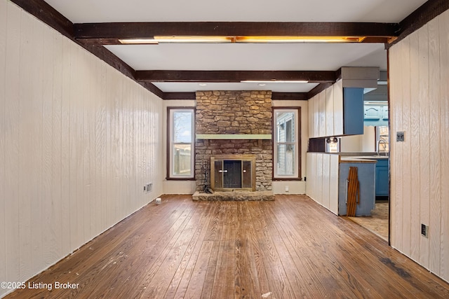 unfurnished living room featuring wooden walls, a fireplace, sink, hardwood / wood-style flooring, and beam ceiling