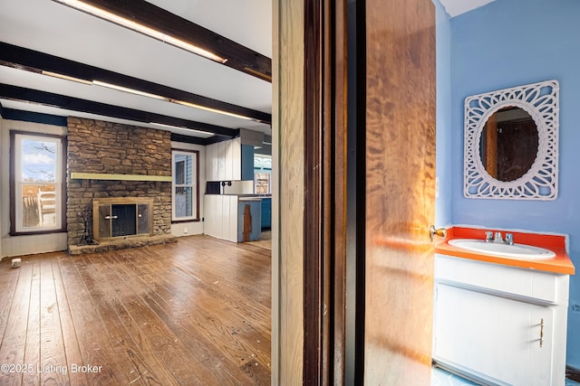 unfurnished living room with sink, hardwood / wood-style floors, a fireplace, and beam ceiling