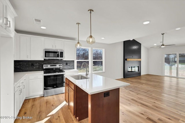 kitchen featuring tasteful backsplash, sink, white cabinets, stainless steel appliances, and a center island with sink