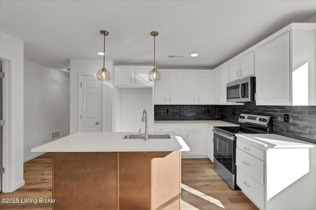 kitchen featuring stainless steel appliances, an island with sink, sink, and white cabinetry