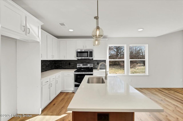 kitchen with appliances with stainless steel finishes, pendant lighting, white cabinetry, sink, and decorative backsplash