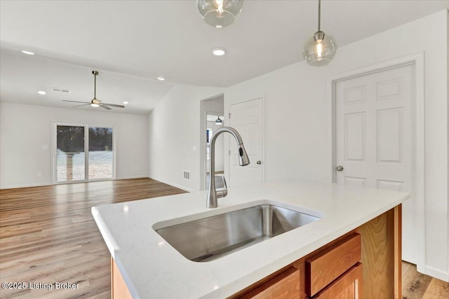 kitchen featuring sink, hanging light fixtures, a kitchen island with sink, ceiling fan, and light hardwood / wood-style flooring