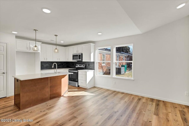 kitchen with pendant lighting, sink, stainless steel appliances, white cabinets, and a center island with sink