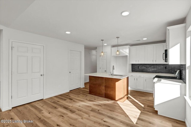 kitchen with sink, range, white cabinets, a center island with sink, and decorative light fixtures